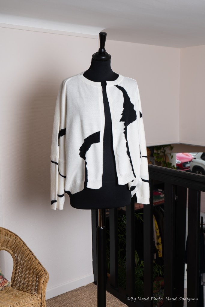 Cardigan écru avec motifs noirs (fermeture par épingle à nourrice). Composition bi-matière 100 % laine / 100 % nylon. Taille M.